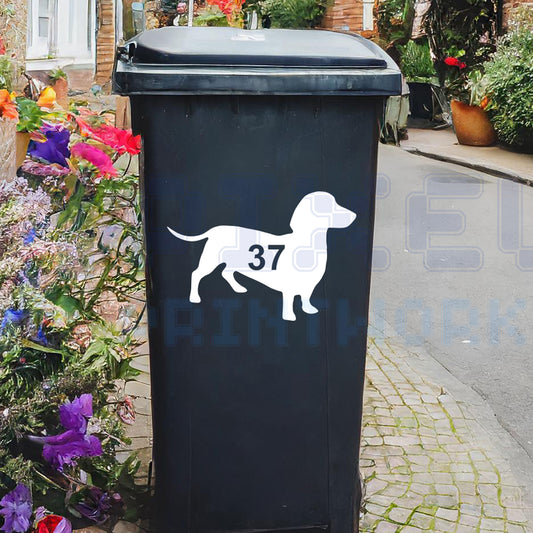 Personalised sausage dog wheelie bin sticker showing a dachshund silhouette with cut-out house number on a bin outside a UK home by Pixel Printworks